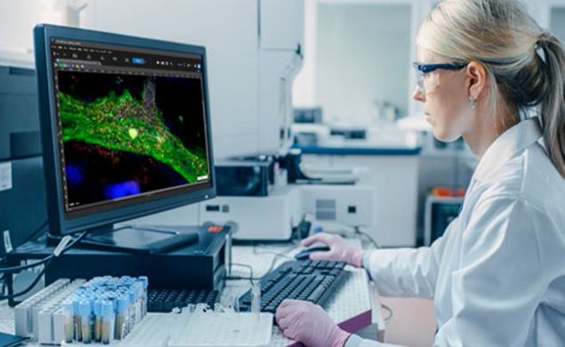 坐在奥林巴斯显微镜前的一位女士在电脑显示器上观察样品